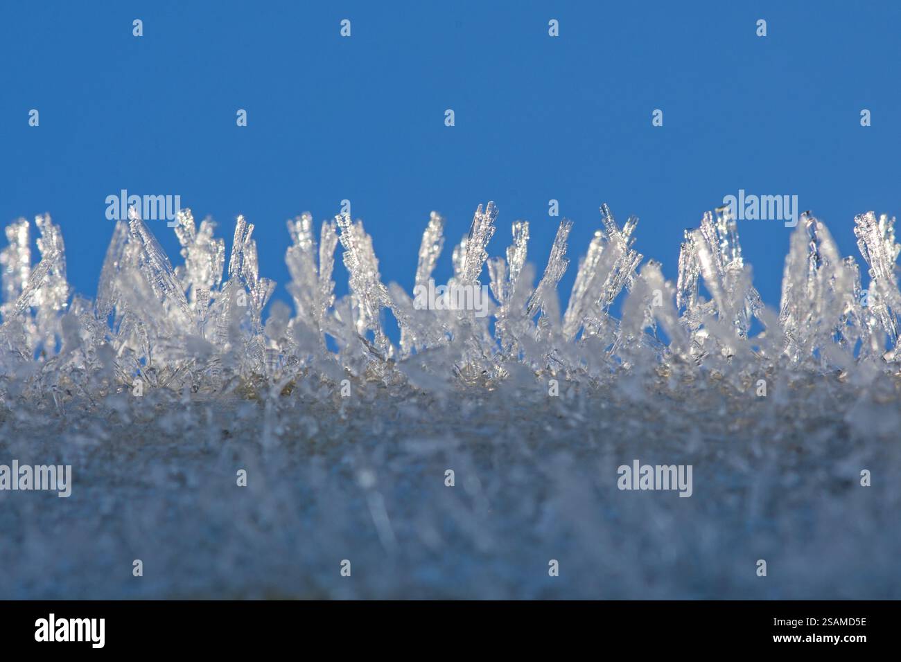 Scharfe weiße Eiskristalle hintereinander vor blauem Himmel Stockfoto