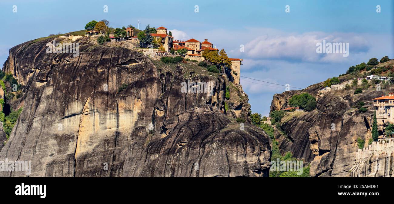 Ein Panoramablick auf eine felsige Klippe mit einem historischen Kloster auf der Spitze, umgeben von üppigem Grün und einem klaren blauen Himmel. Die dramatische Landschaft s Stockfoto