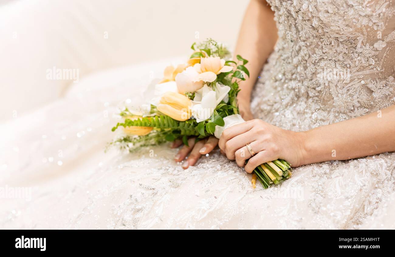 Die Frau trägt ein Hochzeitskleid und hält einen Blumenstrauß. Sie sitzt auf einer Couch Stockfoto