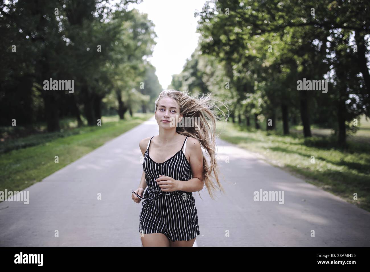 Frau in gestreiftem Outfit, die auf einer leeren Straße zwischen Bäumen läuft Stockfoto