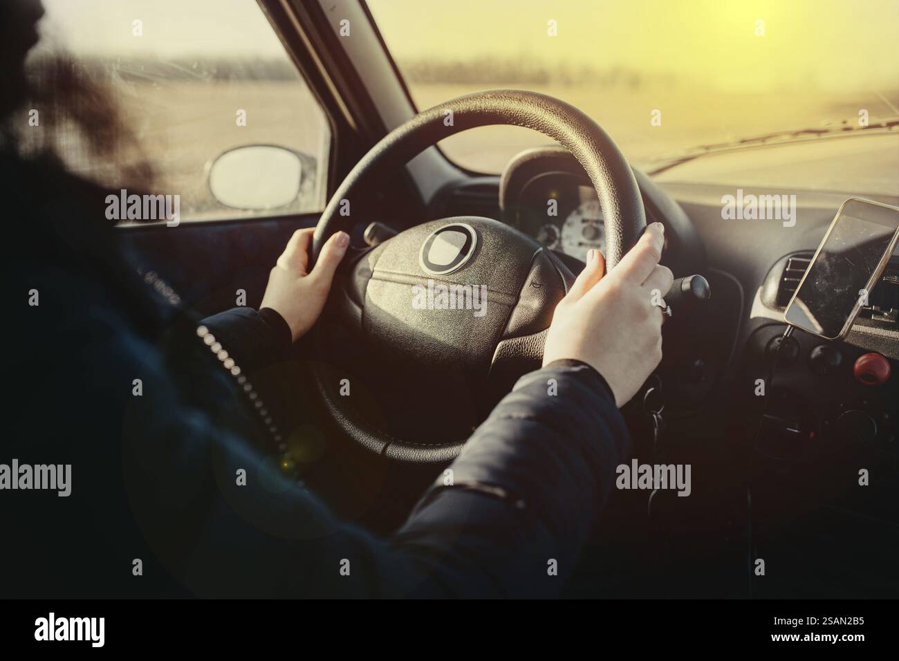 Hände, die während der Fahrt ein Lenkrad halten und Sonnenlicht einströmen Stockfoto