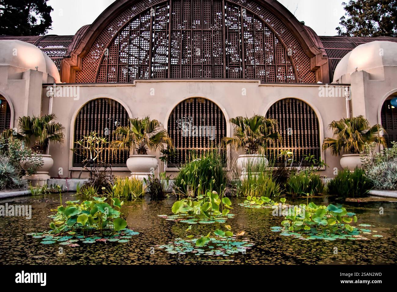 Ein großes Gebäude mit einem Innenhof davor. Der Innenhof hat einen Teich mit Pflanzen und Blumen Stockfoto