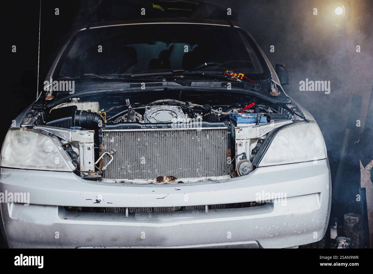 Vorderansicht eines Fahrzeugs mit geöffneter Motorhaube in einer dunklen Garage, die eine nebelige Atmosphäre ausstrahlt Stockfoto