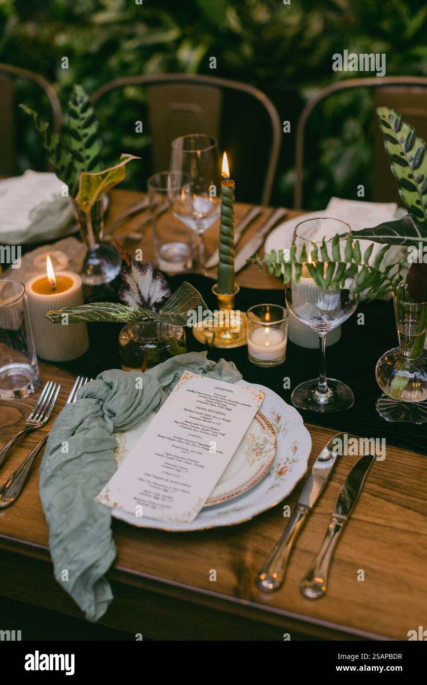 Ein wunderschön gestalteter Tisch bietet elegante Gerichte, flackernde Kerzen und üppiges Grün, was eine warme Atmosphäre für ein intimes Abendessen schafft Stockfoto