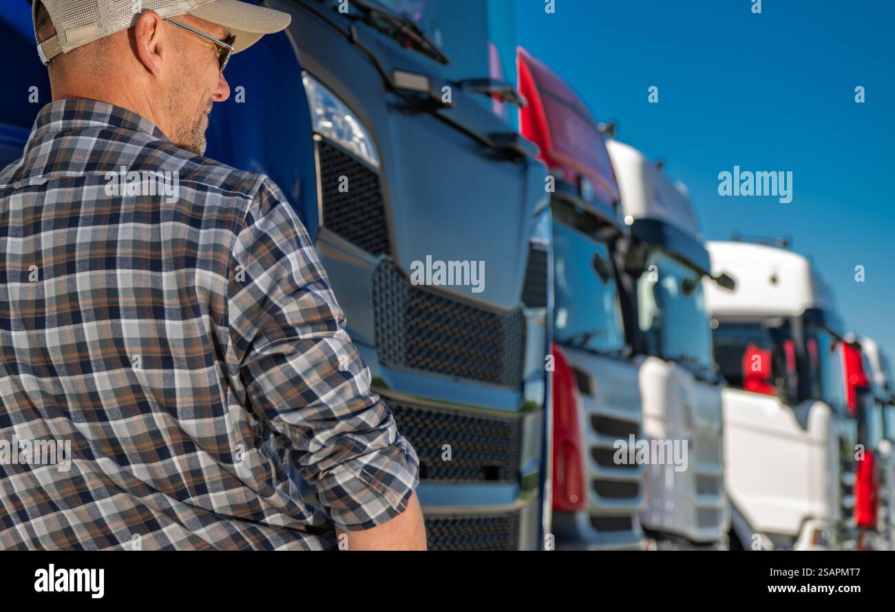 In einem Händlerbetrieb steht ein Mann vor mehreren Lkw und untersucht die Fahrzeuge bei hellem Sonnenlicht. Der Tag ist klar, ohne Wolken. Stockfoto