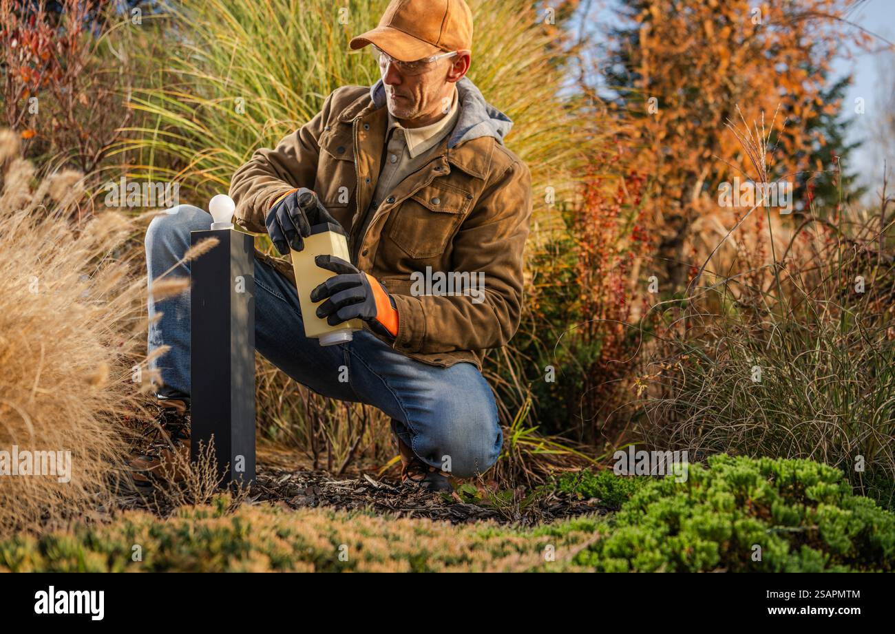 Ein Gärtner pflegt sorgfältig in einem farbenfrohen Herbstgarten und nährt das lebhafte Laub während der Herbstsaison mit einer Sprühflasche. Stockfoto