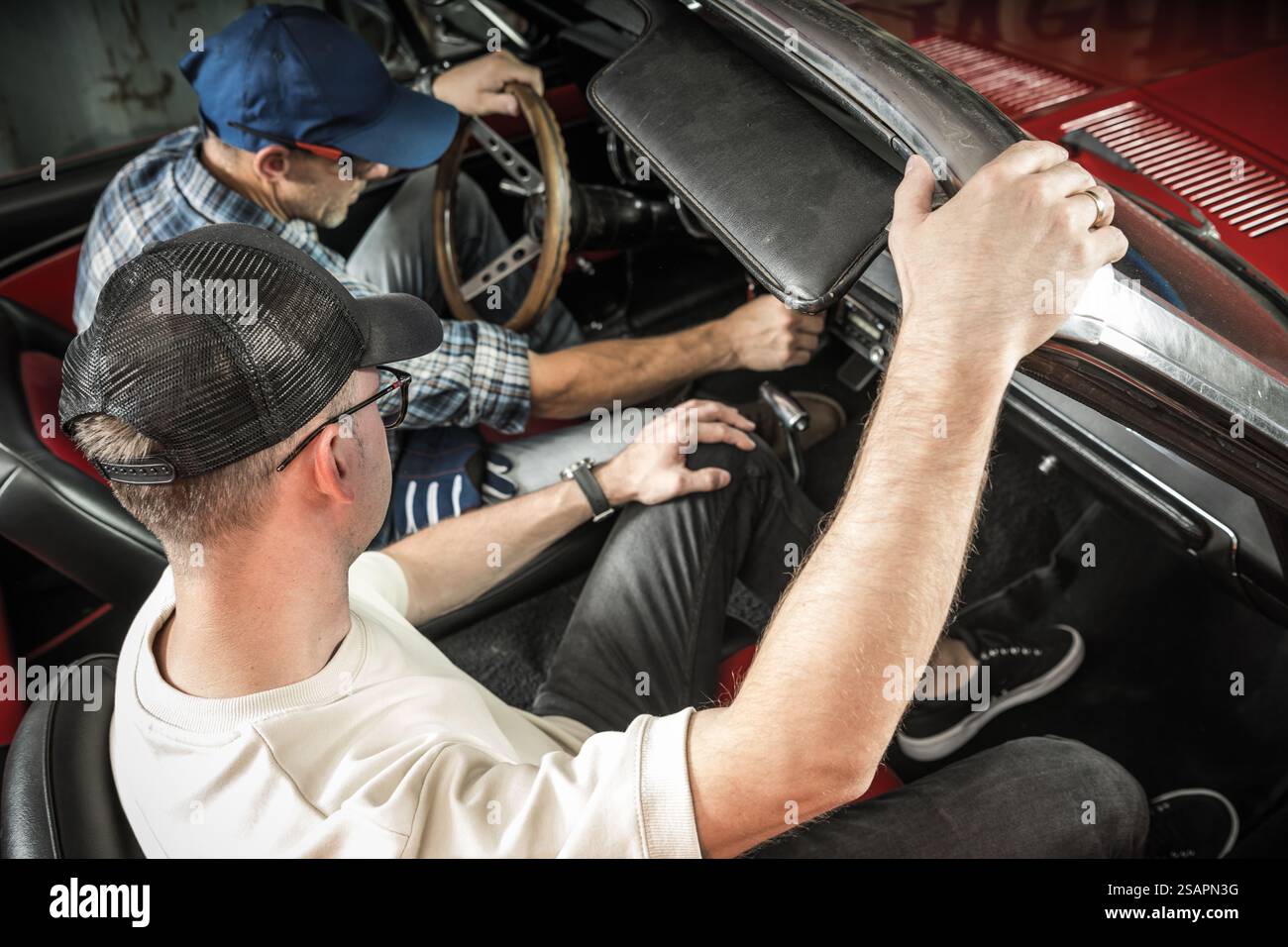 Zwei Mechaniker arbeiten am Innenraum eines Oldtimers zusammen und konzentrieren sich auf Reparaturen in einer Werkstatt, die von Werkzeugen und Ausrüstung umgeben ist. Stockfoto