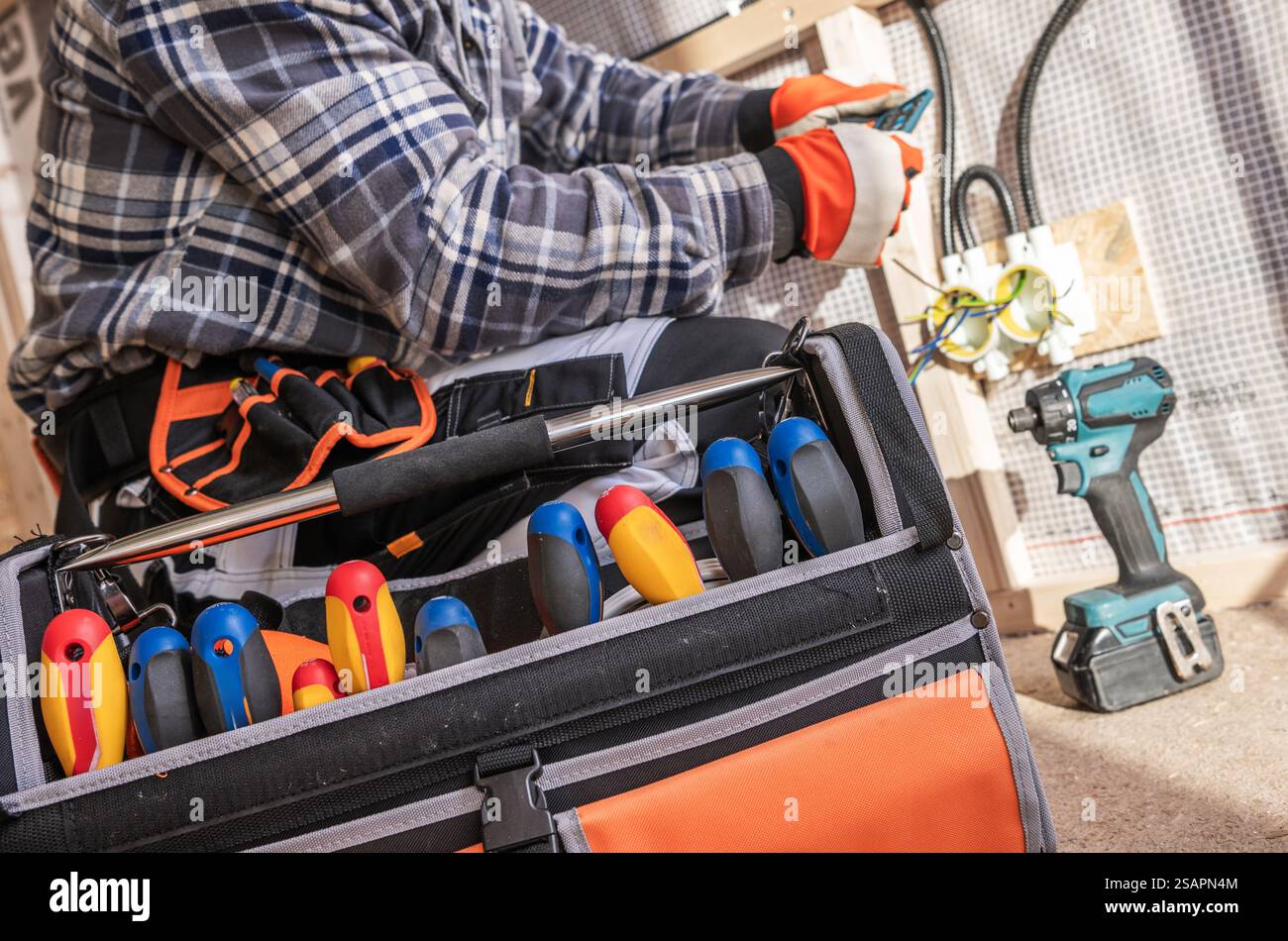 Ein Techniker konzentriert sich darauf, elektrische Leitungen in einem Haus zu reparieren. Er verwendet verschiedene Werkzeuge aus seinem Werkzeugkasten, um fachkundige Arbeit und Sicherheitsvorkehrungen zu demonstrieren Stockfoto