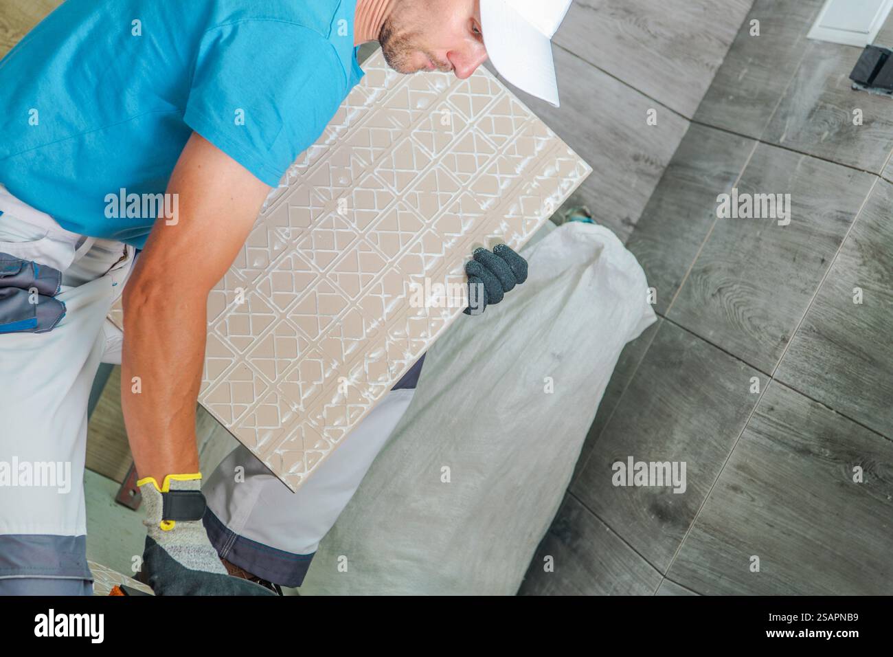 Ein Bauarbeiter installiert gemusterte Fliesen auf dem Boden eines stilvollen Innenraums und zeigt so Fachwissen und Präzision in einer gut beleuchteten Umgebung. Stockfoto