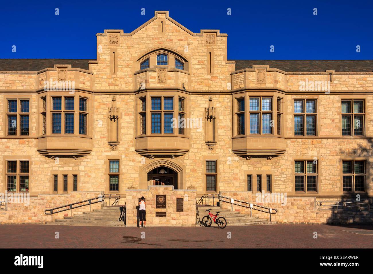 Ein großes Gebäude mit einer Steinfassade und einem Uhrenturm. Eine Frau steht vor dem Gebäude Stockfoto