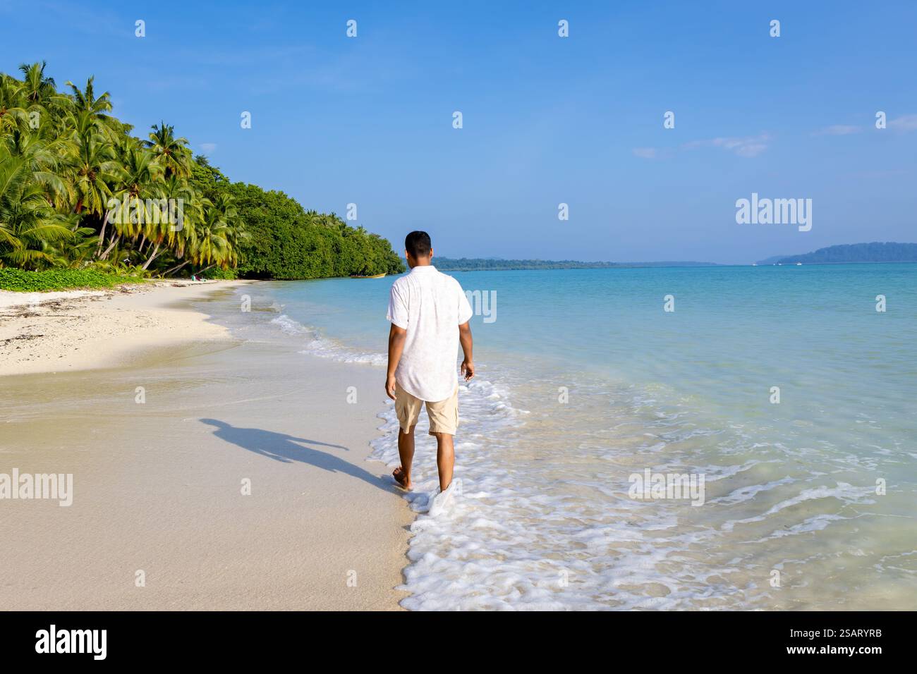 Isolierter Mann, der am unberührten weißen Sandstrand mit sanften Meereswellen am Morgen aus einem flachen Winkel spaziert, wird am Radhanagar Beach auf der Havelock Island aufgenommen Stockfoto