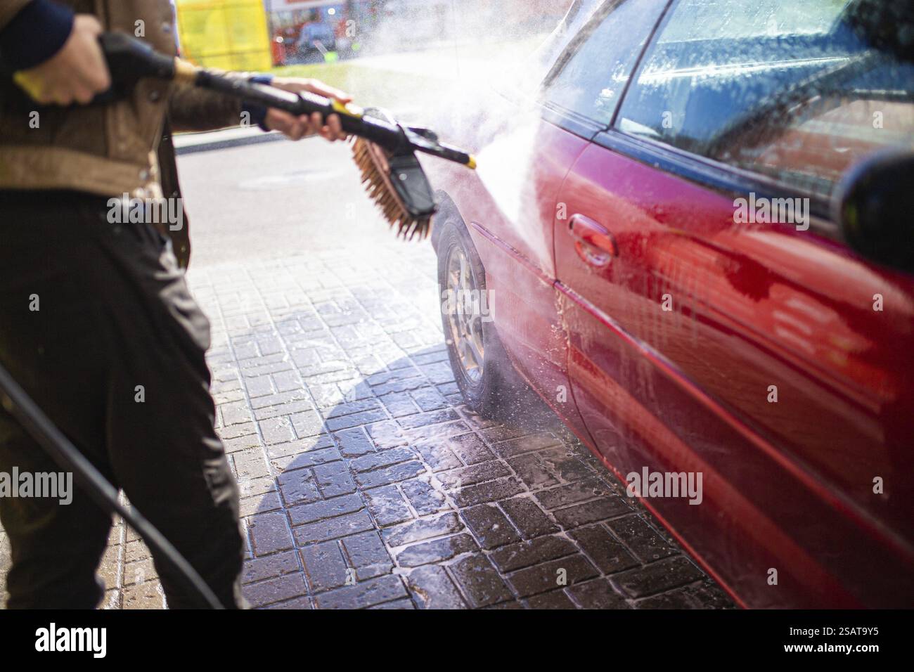 Druckwäsche eines roten Autos auf einer kopfsteingepflasterten Straße im Sonnenlicht Stockfoto