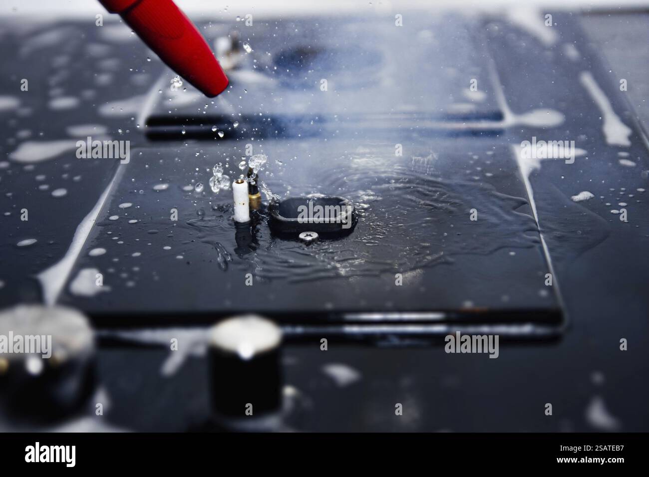 Rote Düse, die Wasserspray auf einen sprudelnden Seifenherd abgibt Stockfoto