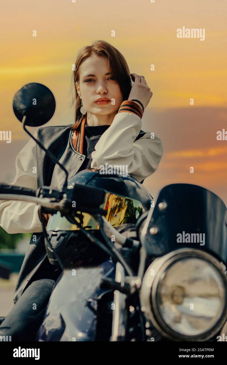 Frau auf einem Motorrad mit Sonnenuntergang Hintergrund, entspannter, traumhafter Ausdruck Stockfoto