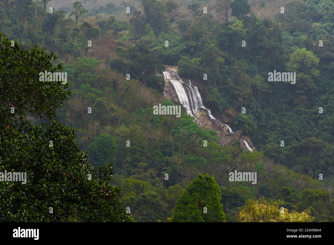 Ein atemberaubender Blick auf einen kaskadierenden Wasserfall inmitten üppiger grüner Berge. Halten Sie die beeindruckende Schönheit der Natur fest Stockfoto