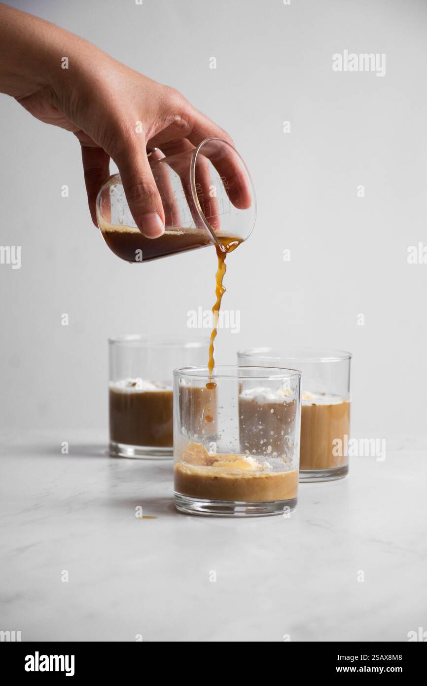 Kaffee wird über drei Gläser mit Vanilleeis gegossen Stockfoto