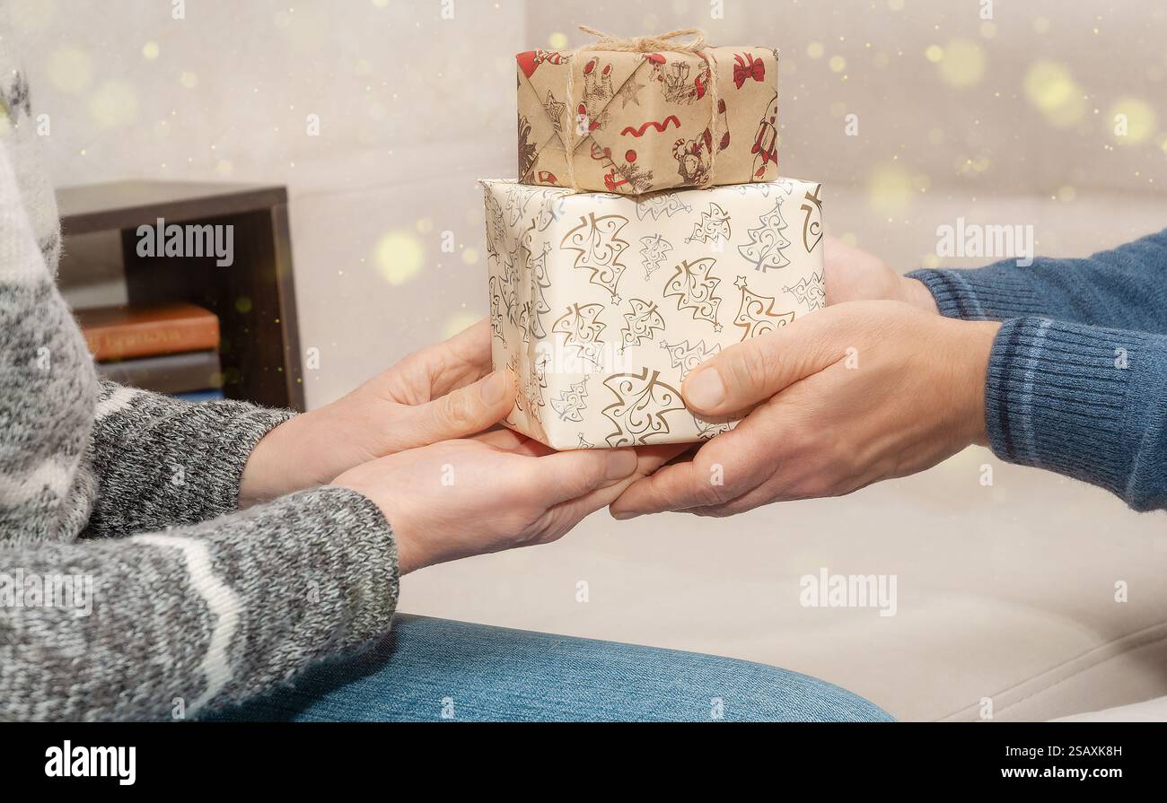 Zwei Personen tauschen wunderschön verpackte Geschenke in einem stilvollen Wohnzimmer mit Wärme und Weihnachtsstimmung aus. Stockfoto
