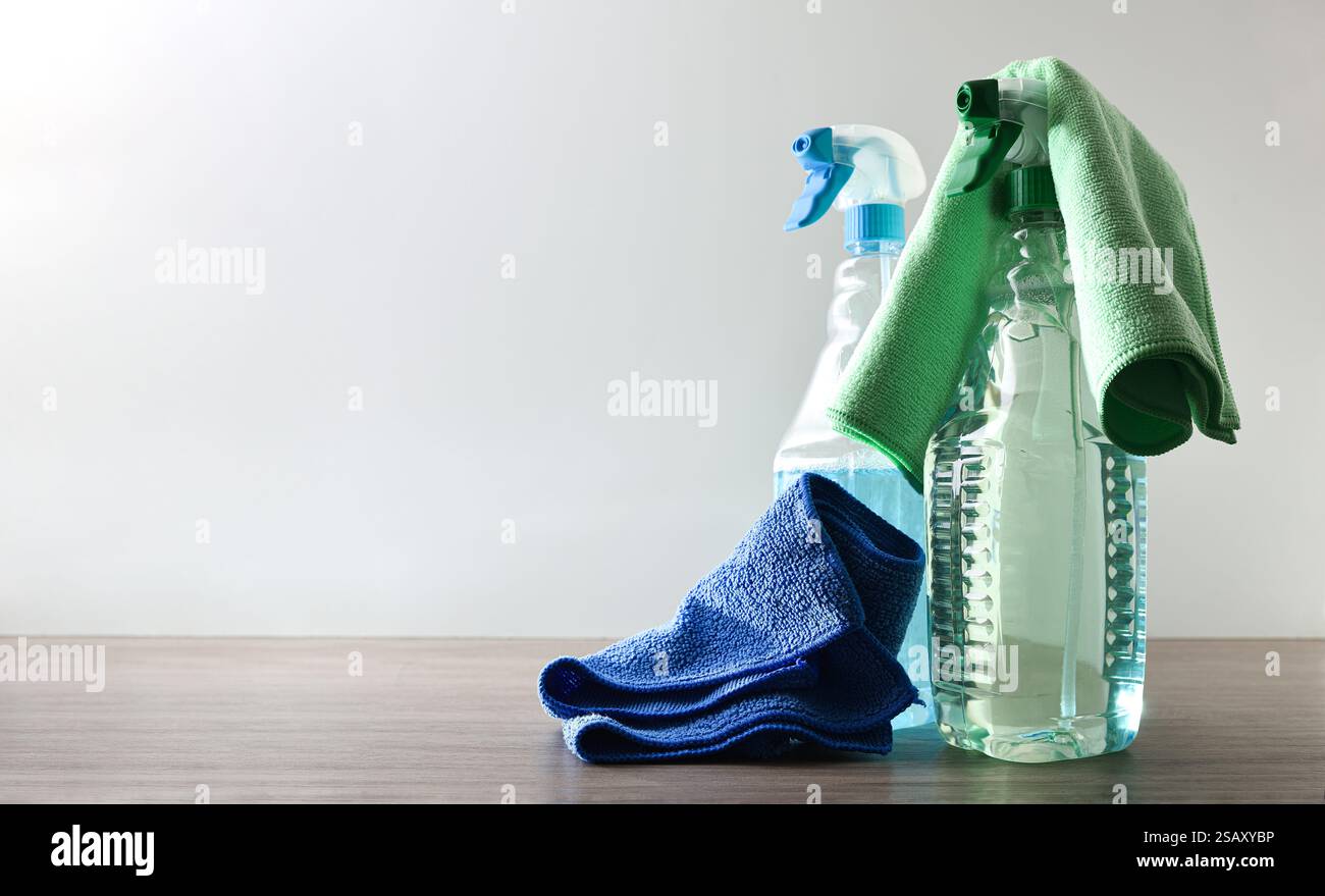 Sprühen Sie Flaschen mit einem allgemeinen Haushaltsreiniger mit Mikrofasertüchern auf Holztisch und weißem isoliertem Hintergrund. Vorderansicht. Stockfoto