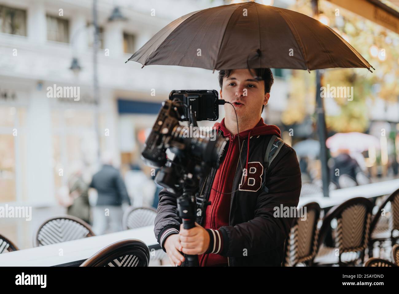 Filmemacher mit Kamera und Schirm, der Momente auf einer Straße der Stadt festnimmt Stockfoto