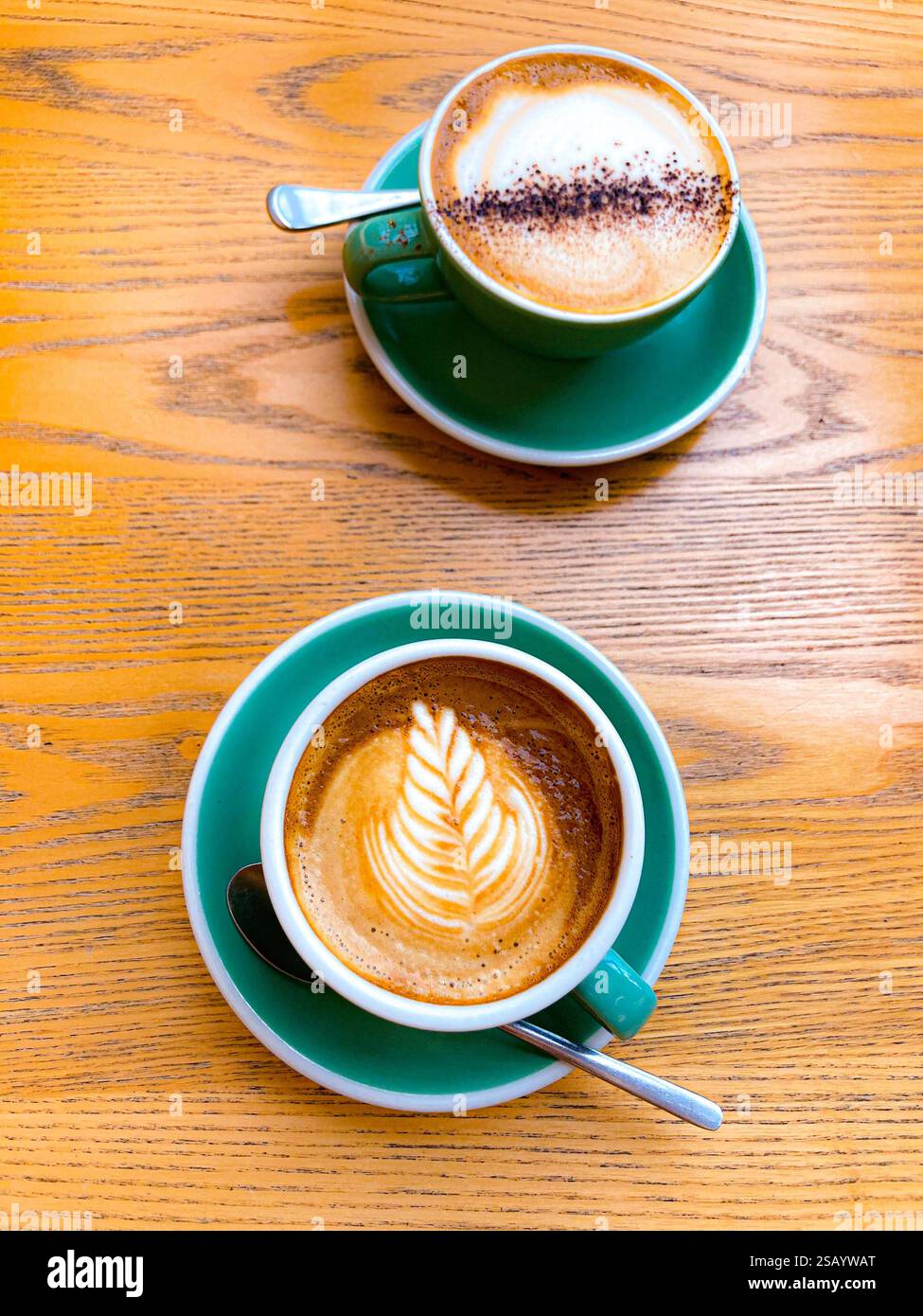 Zwei Kaffeetassen und Teelöffel auf einem bewaldeten Tisch in einem Café Stockfoto
