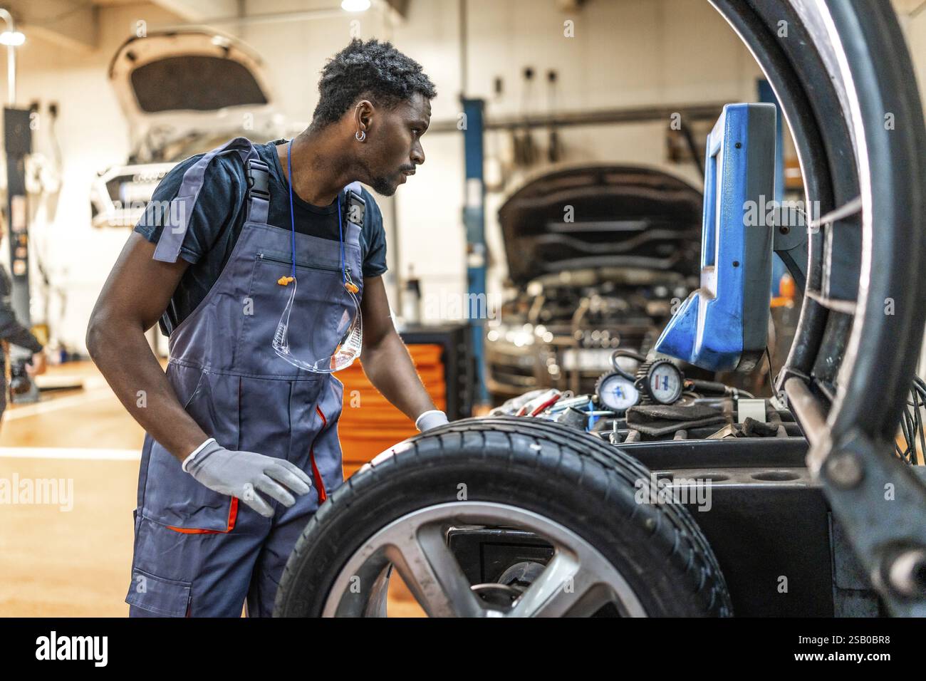 Professioneller Mechaniker, der ein digitales Reifendruckmessgerät während einer Radwartung in einer stark frequentierten Autowerkstatt verwendet Stockfoto