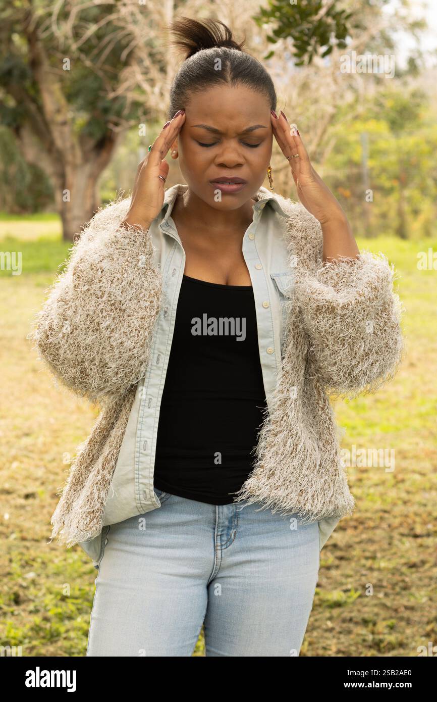 Eine schwarze Frau mit Brille und einem gemütlichen Outfit hält ihren Kopf mit beiden Händen und drückt Frustration und Stress aus. Stockfoto