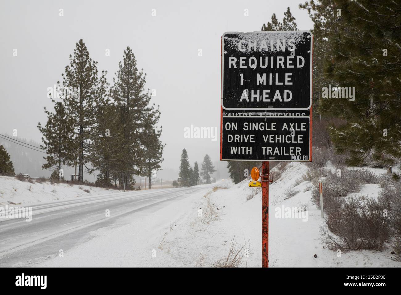 Ketten für alle einachsigen Fahrzeuge beim Ziehen erforderlich – Lassen County, Kalifornien. Winterliches Verkehrssicherheitsschild bei schneebedeckten Bedingungen. Stockfoto