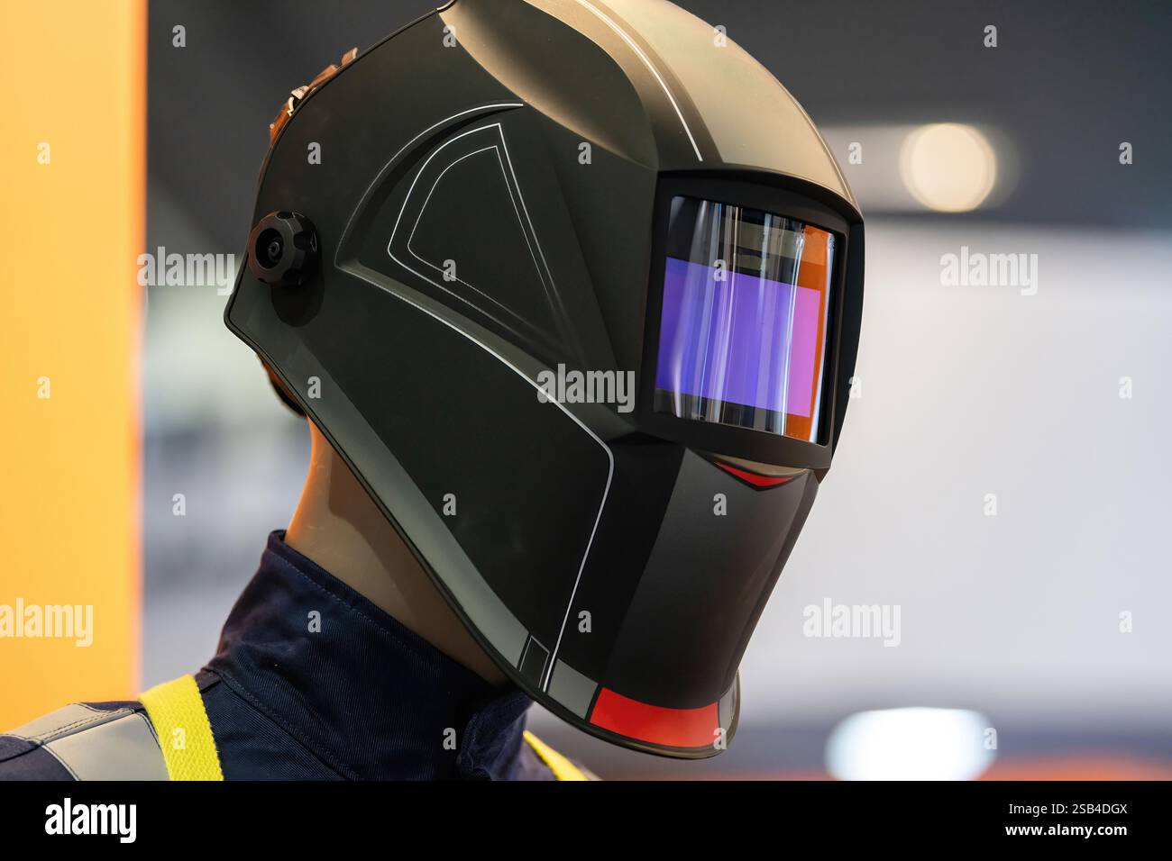 Persönliche Schutzausrüstung (PSA) Schaufensterpuppe mit einem modernen Schweißhelm mit reflektierendem Visier in einer hell beleuchteten industriellen Umgebung. Der Helm verfügt über fortschrittliche Designelemente, die Sicherheit und Technologie betonen. Stockfoto