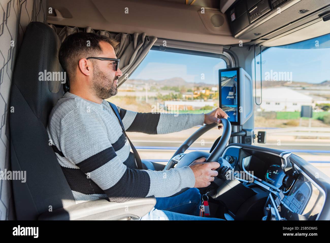Junger Lkw-Fahrer, der einen Lkw auf der Autobahn fährt, von der Kabine aus gesehen, mit Blick auf die Straße. Stockfoto