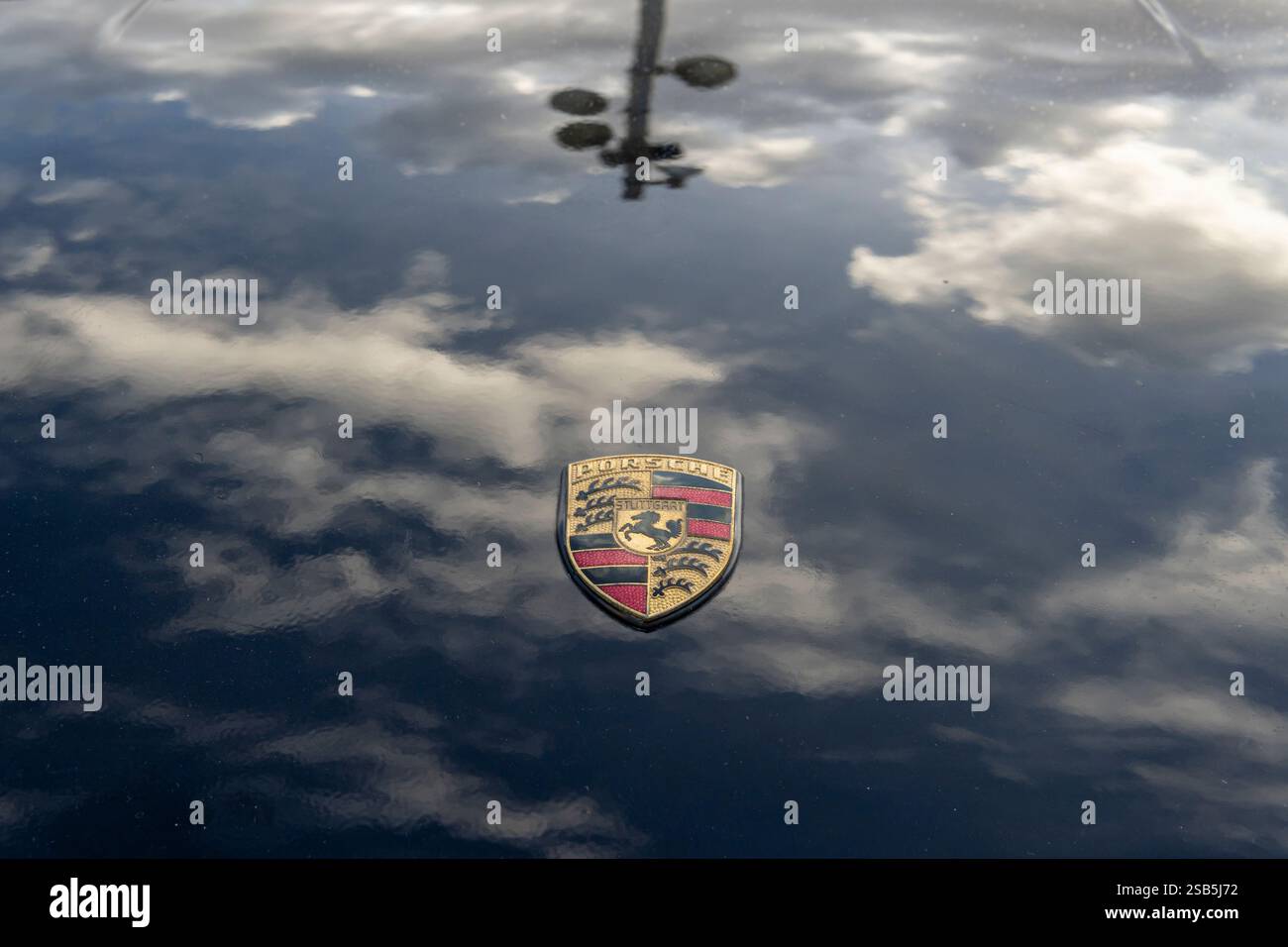 Felanitx, Spanien; 20. oktober 2024: Nahaufnahme des Logos der Luxuswagenmarke Porsche auf einer schwarzen Motorhaube, die einen Wolkenhimmel reflektiert Stockfoto
