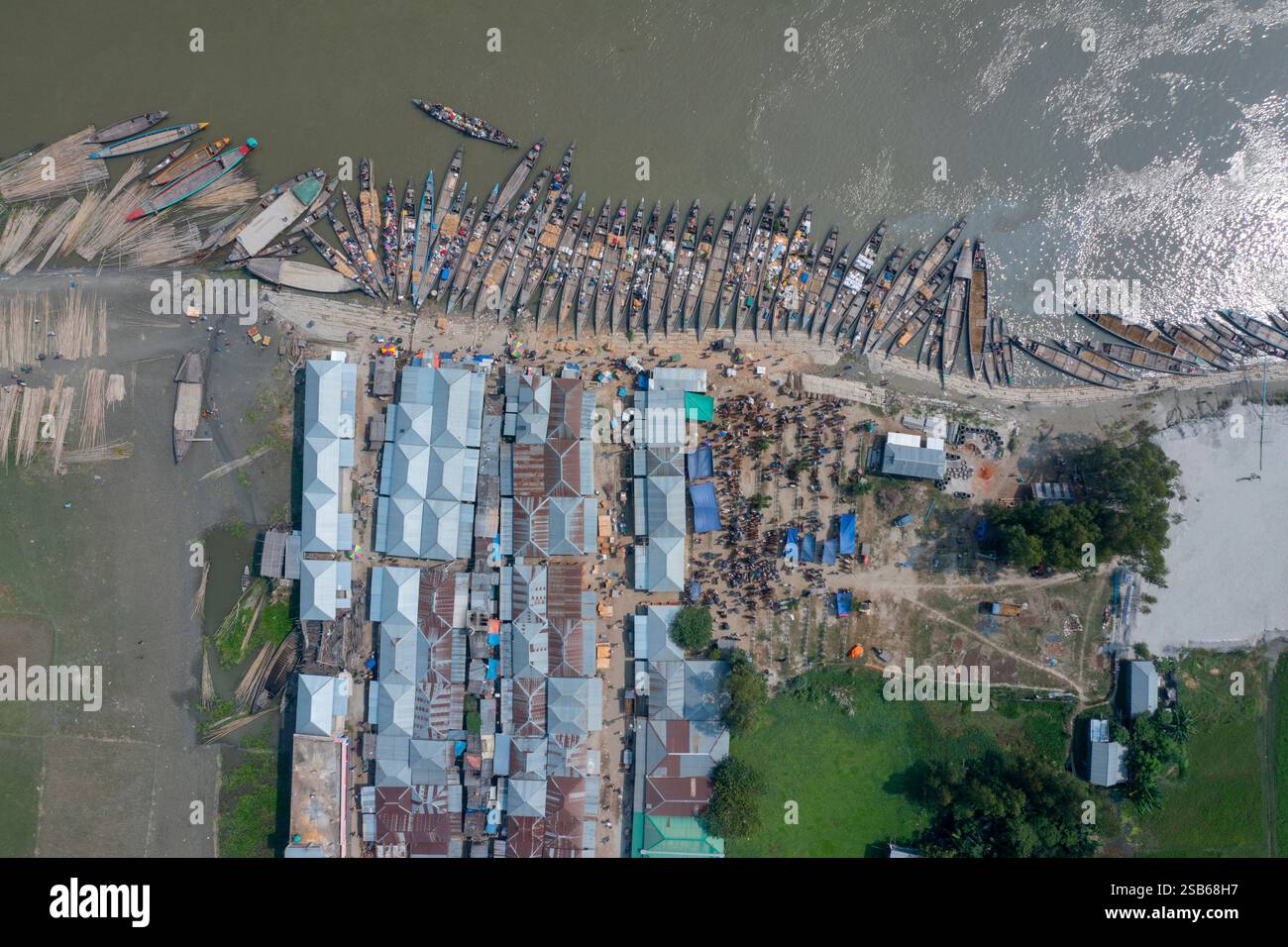 Blick aus der Vogelperspektive auf den belebten Basar am Flussufer Nakalia mit einer Flotte von Booten, die am Ufer des Brahmaputra River in Bera, Pabna, ankern. Stockfoto Blick aus der Vogelperspektive auf den belebten Basar am Flussufer Nakalia mit einer Flotte von Booten, die am Ufer des Brahmaputra River in Bera, Pabna, ankern. Stockfoto