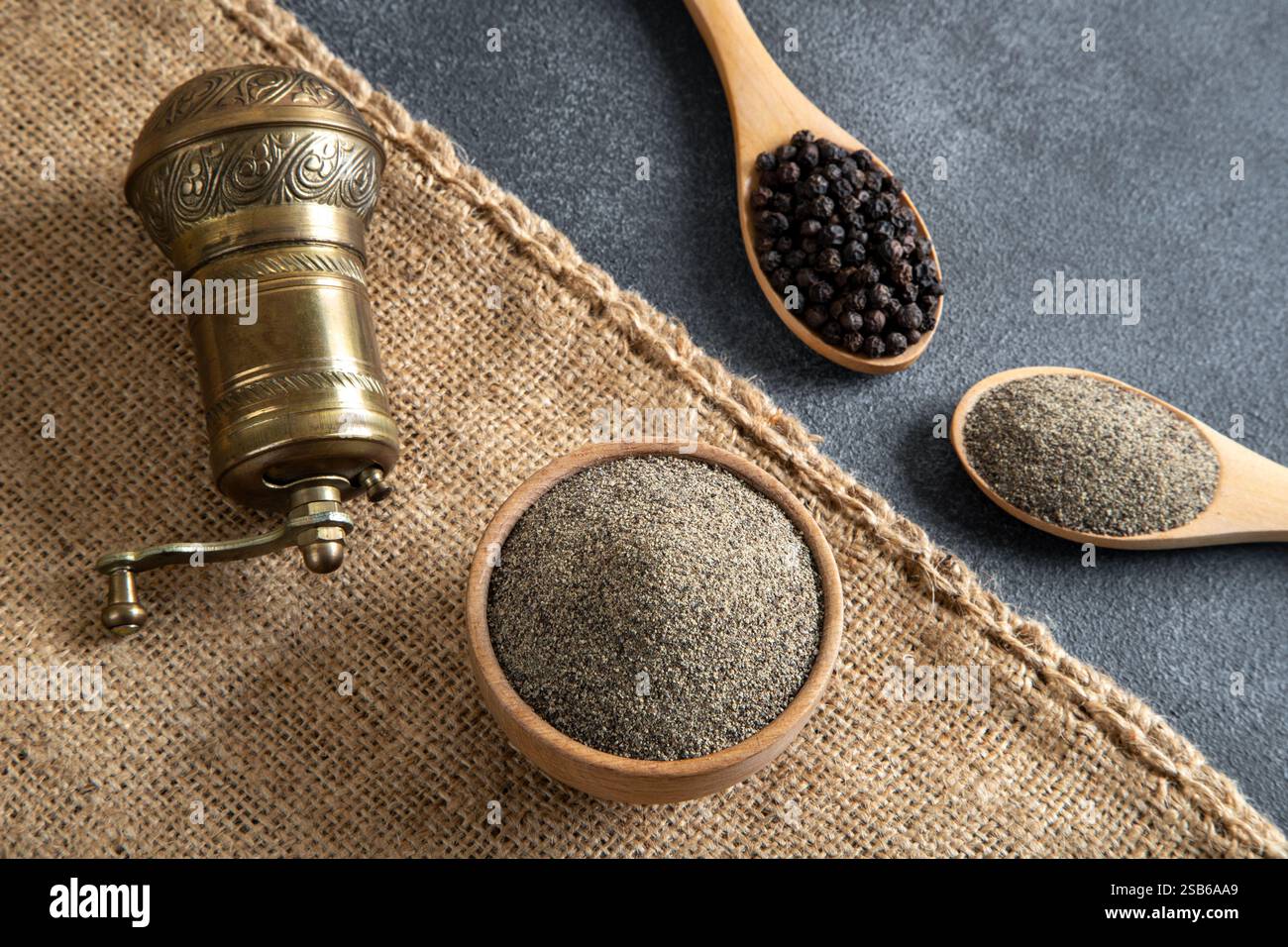 Schüsseln mit schwarzen Pfefferkörnern auf schwarzem Hintergrund und eine Metallschleifmaschine Stockfoto