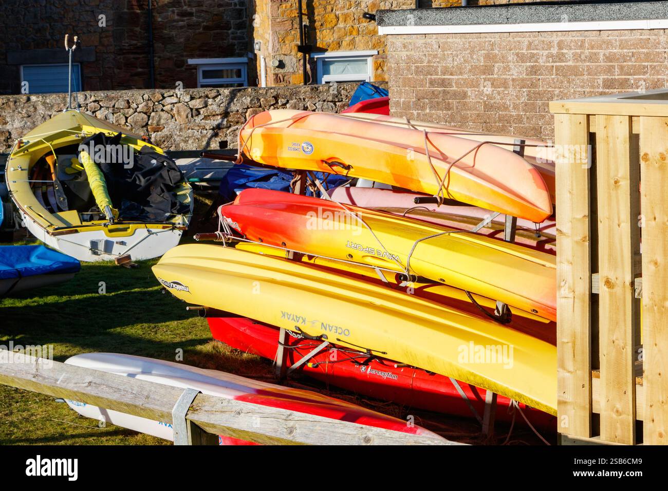 Farbenfrohe Kajaks auf einem Rasen in der Nähe eines Gebäudes, bereit für Outdoor-Wasserabenteuer und Freizeitaktivitäten in der Bucht northumberland uk Stockfoto
