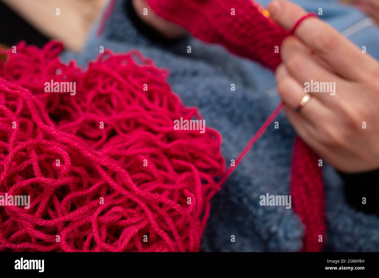 Roter, verwickelter Garn mit defokussierten Frauenhänden, Häkelnadel und weichem Fokus Stockfoto
