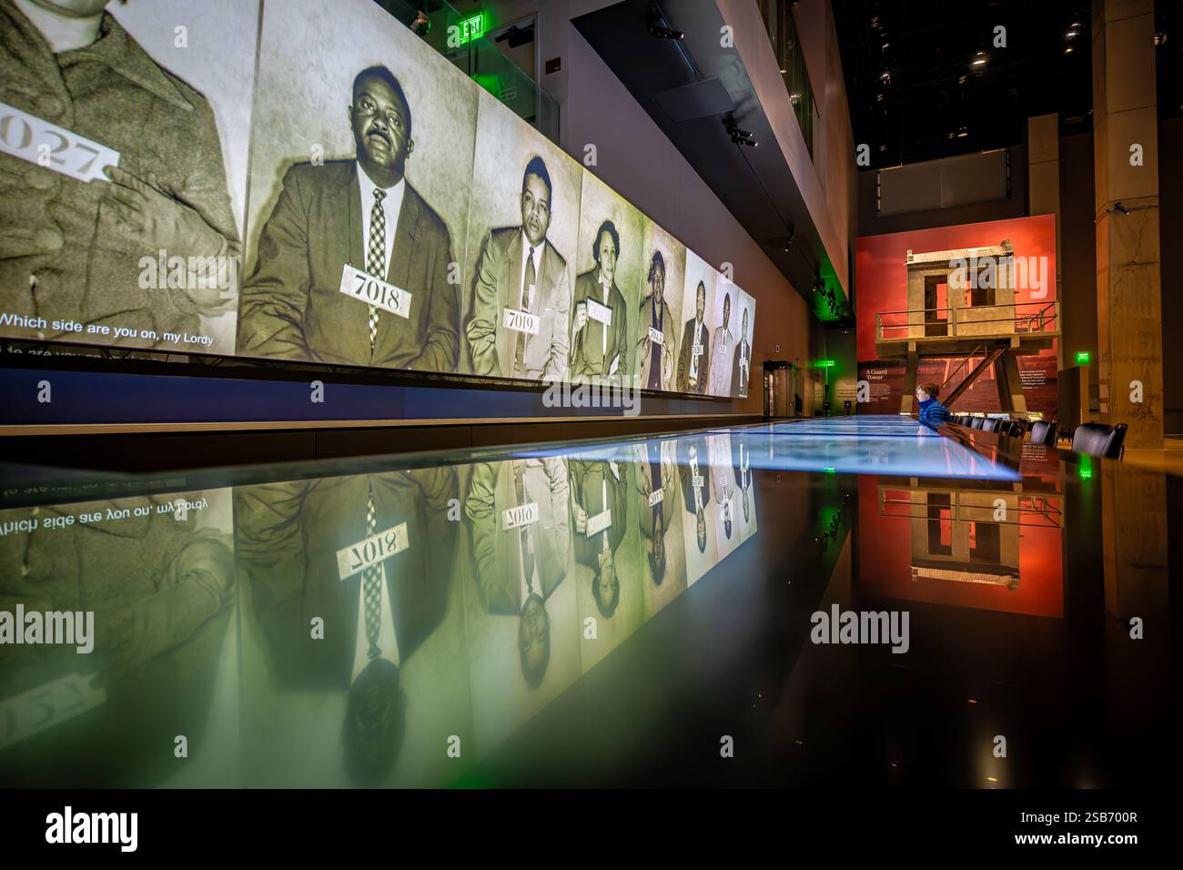 Greensboro Lunch Counter Sit-ins-Ausstellung im National Museum of African American History and Culture in Washington DC | WASHINGTON D.C., Vereinigte Staaten — Fahndungsfotos von Demonstranten der Bürgerrechte leuchten über einem reflektierenden schwarzen Zähler im National Museum of African American History and Culture, Teil einer Galerie über den Widerstand der Jim Crow-Ära. In der Nähe befindet sich ein Wachturm aus dem Louisiana State Penitentiary in Angola, eines der großen Artefakte des Museums, das während der Bauarbeiten im Jahr 2013 in das Gebäude eingebracht wurde. Ein Kind untersucht die Anzeige vom Rand des Wassers aus. Stockfoto