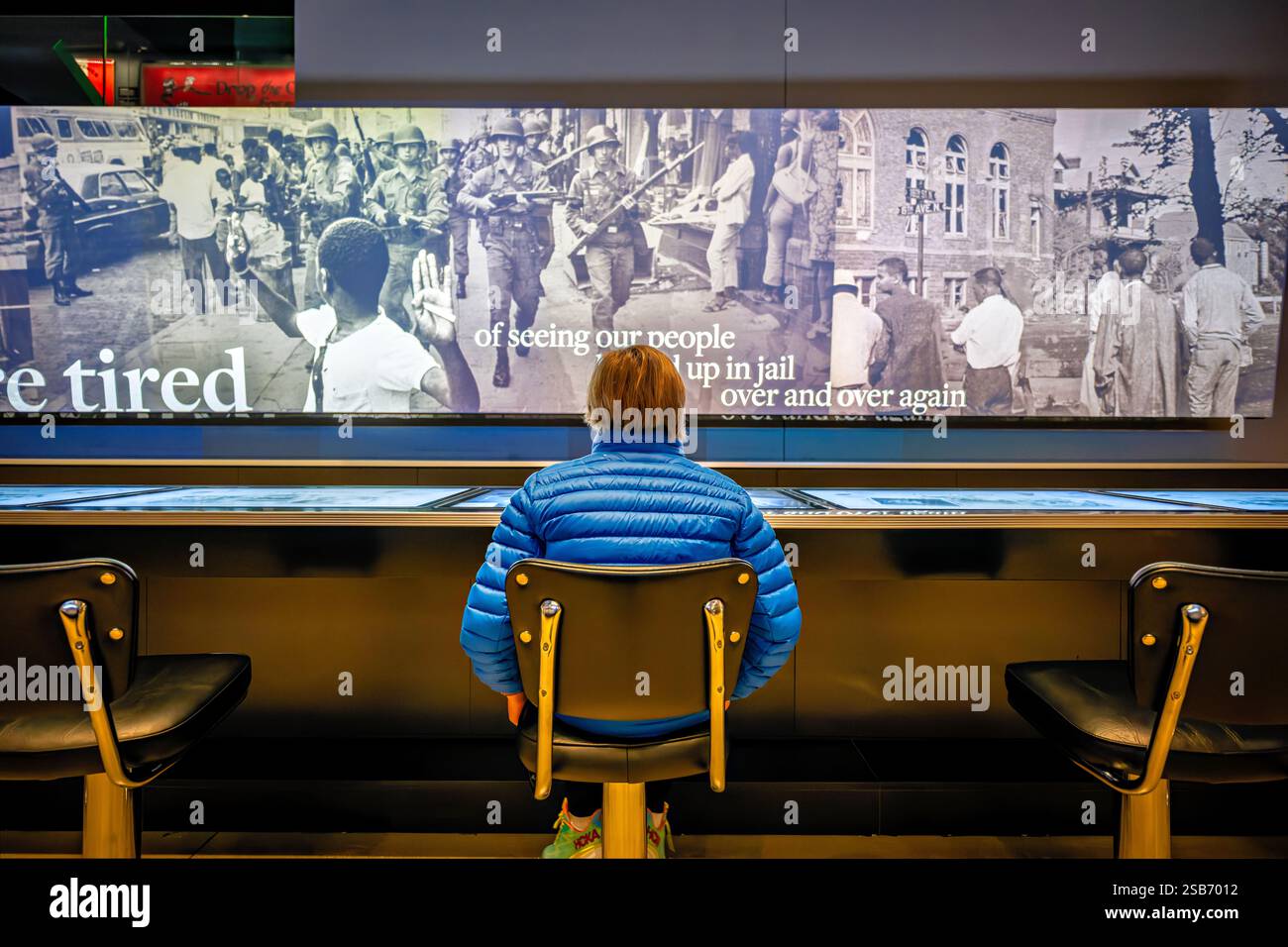 Greensboro Sit-ins Exhibit National Museum of African American History in Washington DC | WASHINGTON D.C., Vereinigte Staaten – Ein Besucher sitzt vor einer Wandmontage von Fotografien aus der Zeit der Bürgerrechte im National Museum of African American History and Culture, Teil einer interaktiven Ausstellung über Segregation und Widerstand im amerikanischen Süden. Auf der Touchscreen-Station können Besucher Archivbilder und Zeugnisse aus der Zeit erkunden, darunter Szenen von Truppen der Nationalgarde, die während der Unruhen der 1960er Jahre eingesetzt wurden. Die Ausstellung verankert die unterirdischen Geschichtsgalerien des Museums. Stockfoto
