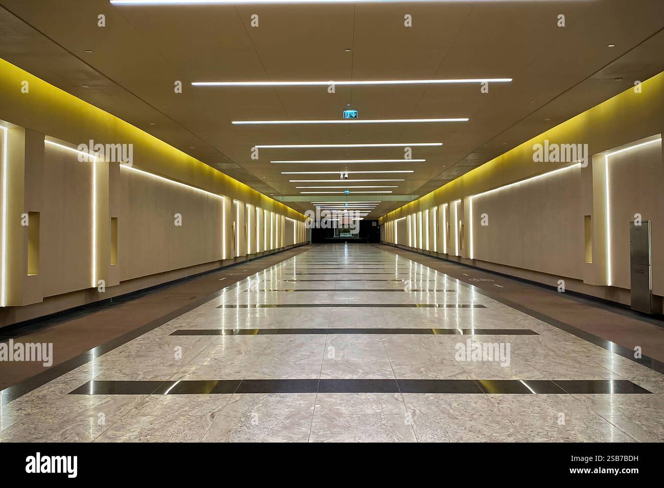 Ein moderner unterirdischer Fußgängertunnel mit eleganter Beleuchtung, Marmorboden und futuristischem Design, der einen geräumigen und beleuchteten Gang schafft. Stockfoto