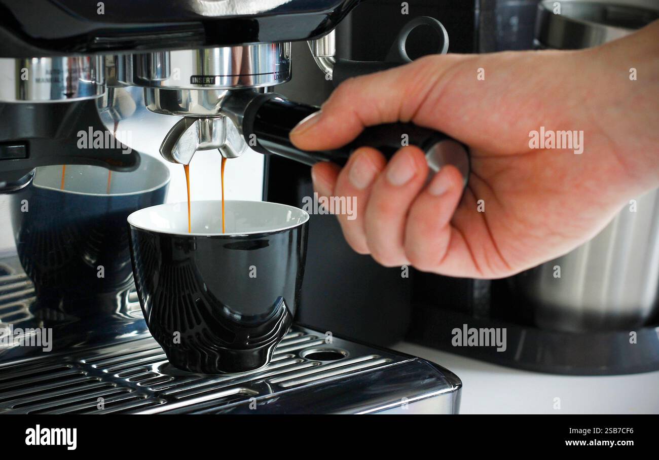 Nahaufnahme einer männlichen Hand, die einen Portafilter hält und zu Hause mit einer modernen Kaffeemaschine frischen aromatischen Kaffee zubereitet. Machen Sie eine Tasse Kaffee Stockfoto