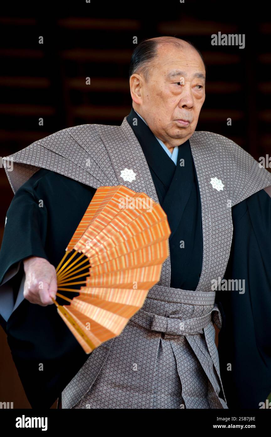Ein Künstler in traditioneller Noh-Tracht, der Fan hält, führt während eines Kyogen-Stücks im Yasaka Jinja-Schrein in Kyoto, Japan, eine Bewegung auf der Bühne aus. Stockfoto