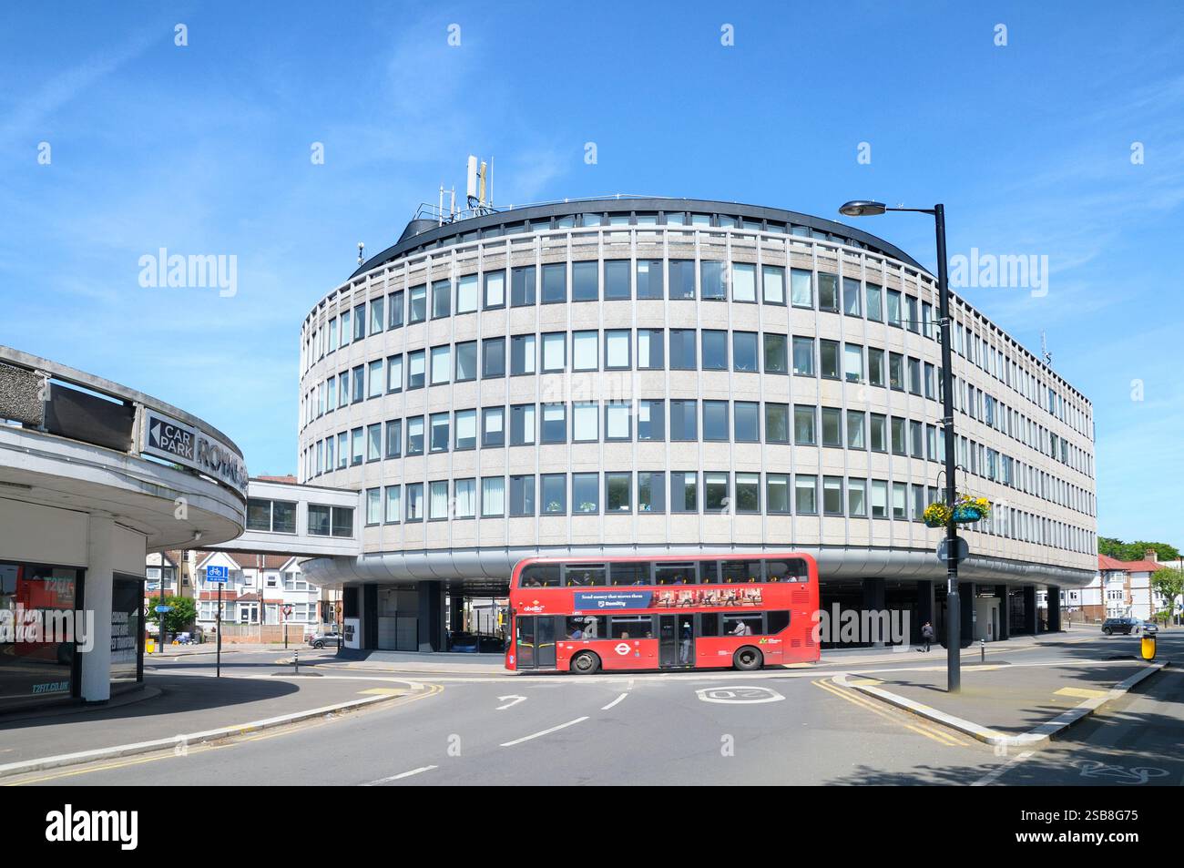 Roter Doppeldeckerbus, der am modernistischen Wahrzeichen Capella Court (ehemals VW Volkswagen Building), Purley, London Borough of Croydon, England, Großbritannien, vorbeifährt Stockfoto