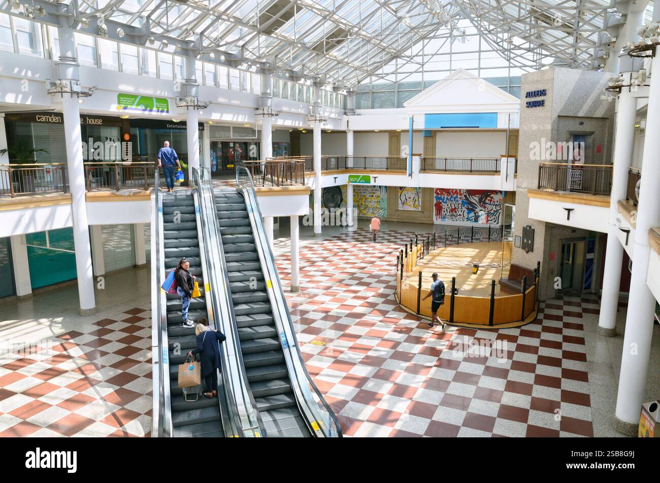 Innenraum des Whitgift Shopping Centre (eröffnet 1970) mit rot-weißen karierten Fliesen und Rolltreppe, die Personen zwischen den Etagen bewegt, Croydon, England, Großbritannien Stockfoto