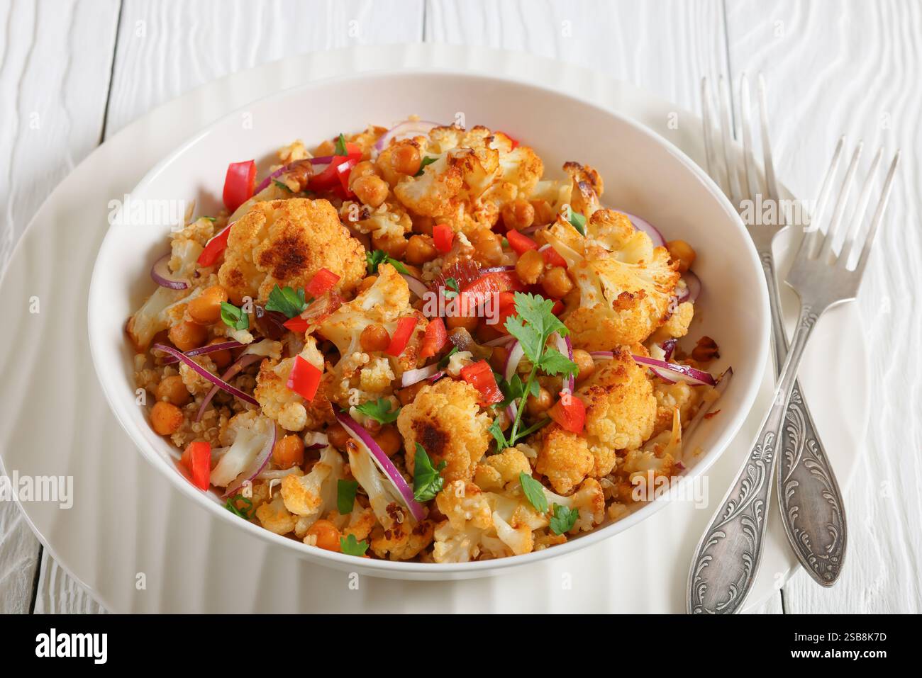 Gebratener Blumenkohl-Kichererbsen-Quinoa-Salat mit Walnüssen, rotem Pfeffer, Zwiebeln und Koriander in einer weißen Schüssel, Nahaufnahme Stockfoto
