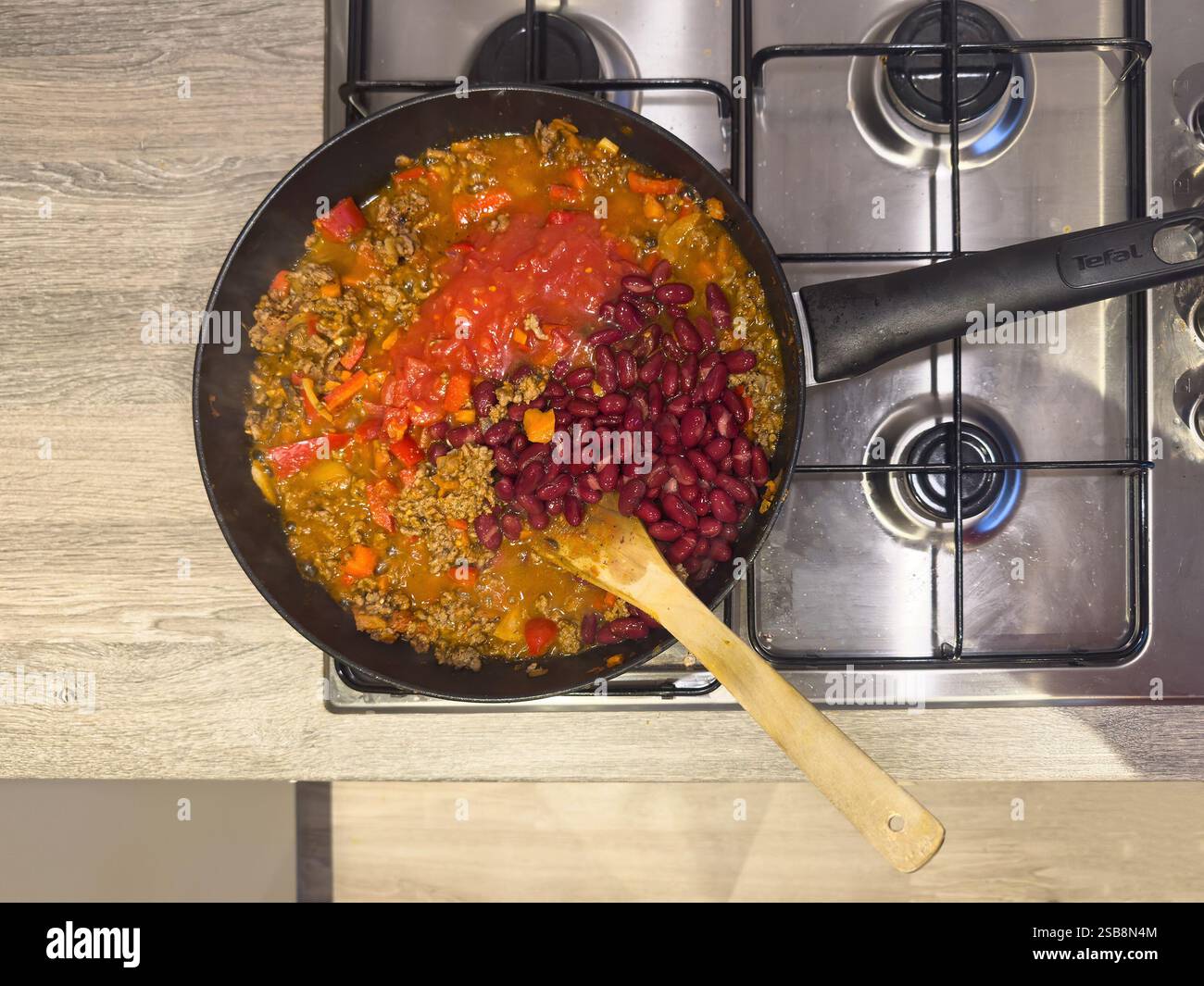Großer Wok und Mann kochen und rühren ein gehacktes Rindfleisch Chili con carne auf einem Herd oder Herd Stockfoto