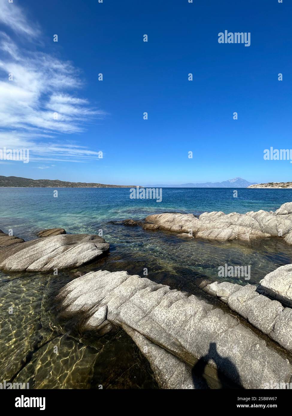 Kristallklares türkisfarbenes Wasser und zerklüftete felsige Küste unter einem leuchtend blauen Himmel, die die ruhige Schönheit einer mediterranen Meereslandschaft einfangen. - Smartphone-aufgenommenes Stockfoto