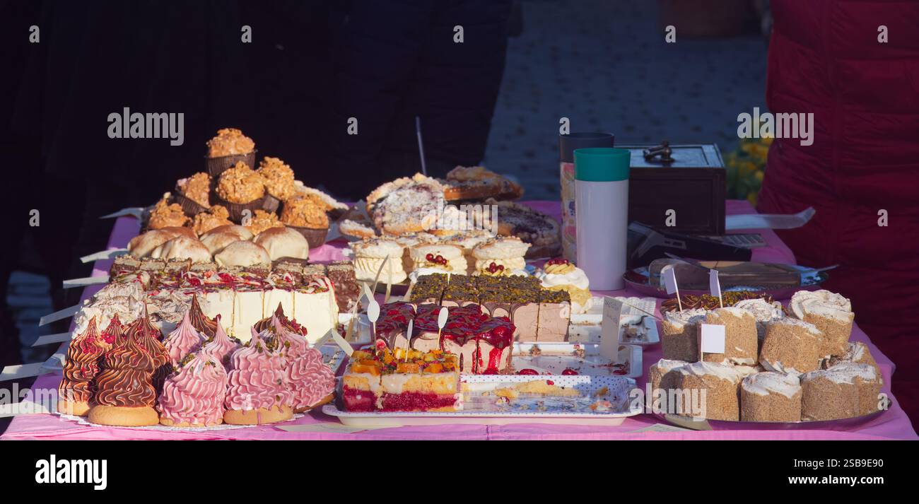 Verschiedene köstliche Gebäckstücke und Kuchen, die auf einem Tisch unter aufgehender Sonne bei einem Treffen im Freien wunderschön angeordnet werden, mit lebhaften Farben und Appetit Stockfoto
