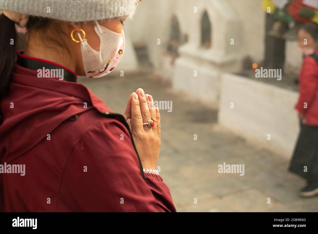 Eine Frau in kastanienbraunem Kleid und Wollmütze betet in der Boudhanath Stupa in Kathmandu. Stockfoto