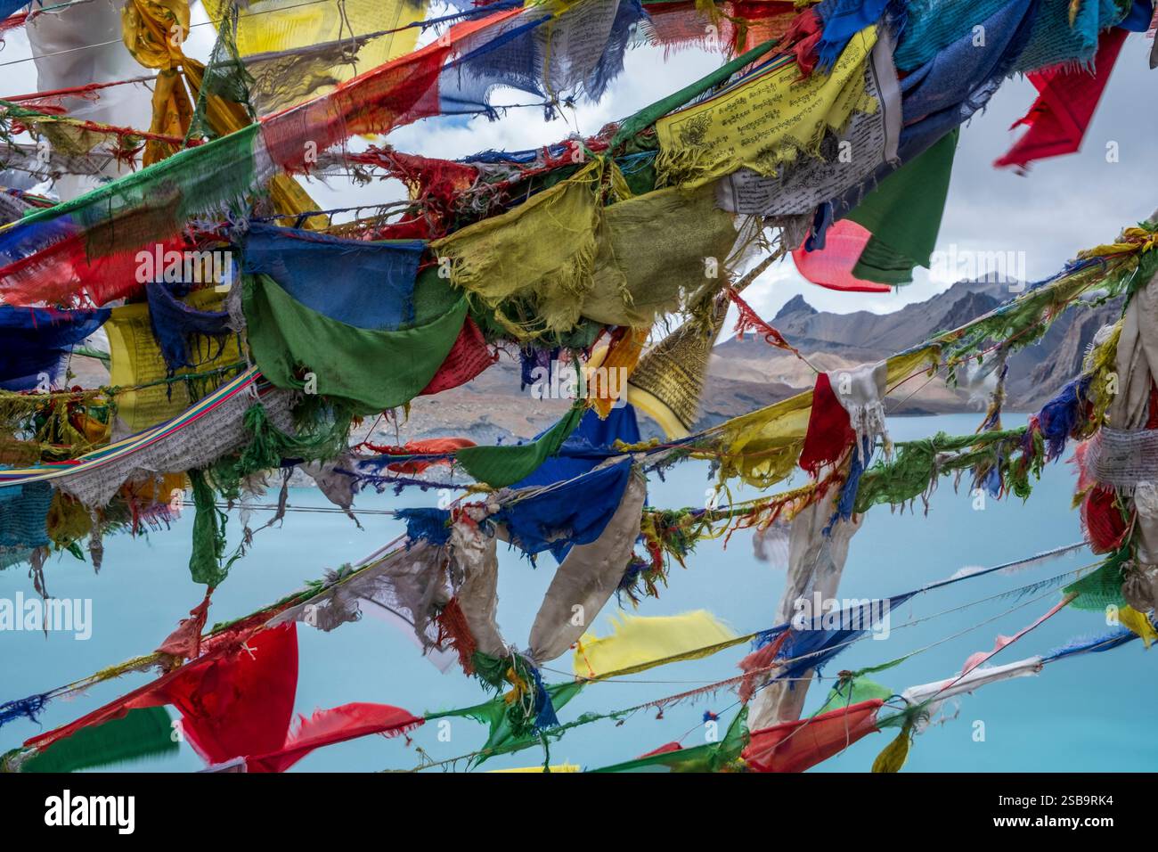 Zerrissene alte Gebetsfahnen flattern im Wind und Schnee über dem Tilicho-See. Stockfoto