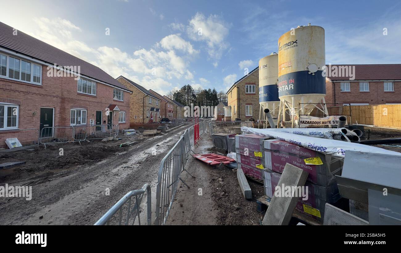 Eine schlammige, unbefestigte Straße führt durch eine neue Wohnsiedlung im Bau. Unvollendete Backsteinhäuser säumen die Straße entlang der Baumatte Stockfoto