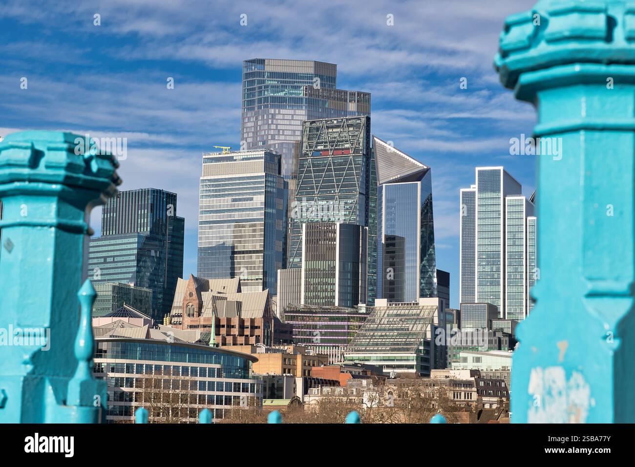 Moderne Wolkenkratzer und ältere Gebäude in London, betrachtet durch blaublaues Brückengeländer unter einem teilweise bewölkten blauen Himmel. Das Bild zeigt eine Mischung aus AR Stockfoto