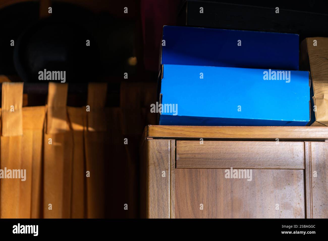 Eine blaue Box auf einem Holzschrank, mit sanfter Beleuchtung, die die Texturen hervorhebt. Im Hintergrund befinden sich Holzvorhänge und dunkle Schatten, c Stockfoto